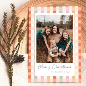 May include: Christmas card with a family photo inside a white border, surrounded by a colorful plaid pattern in orange, pink, and green. The text "Merry Christmas" and "The Fraziers | 2025" are printed on the card.