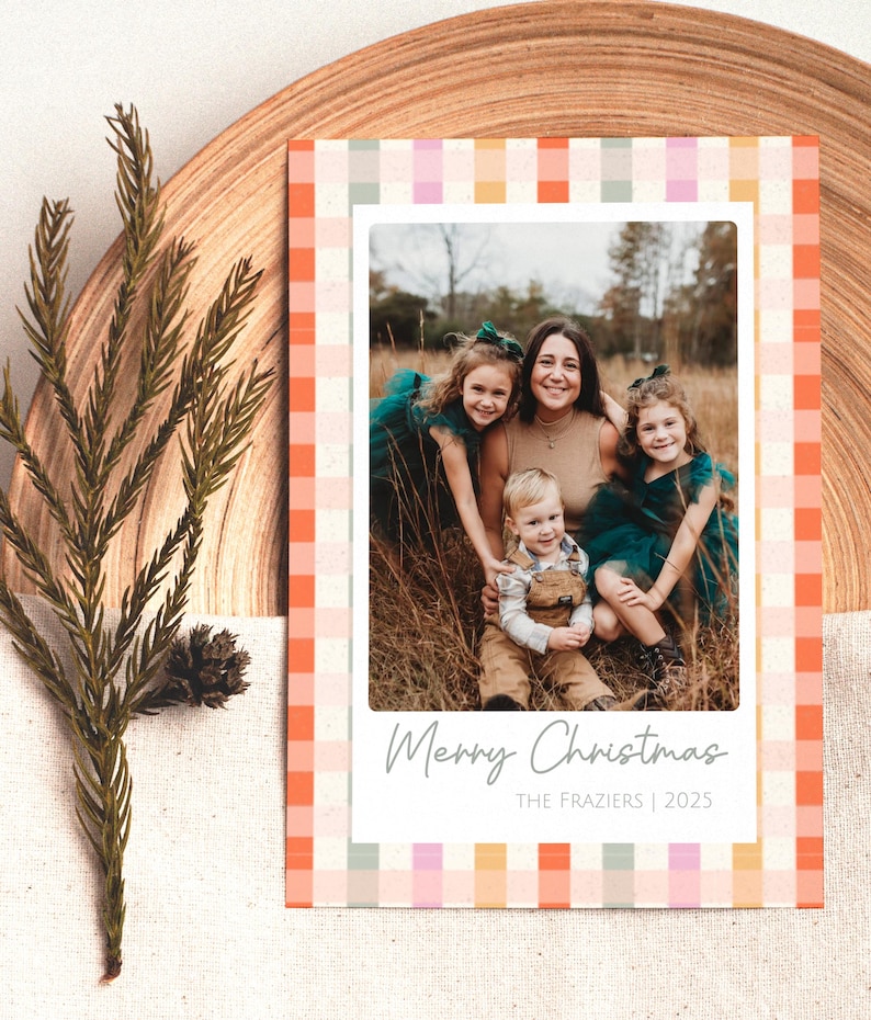 May include: Christmas card with a family photo inside a white border, surrounded by a colorful plaid pattern in orange, pink, and green. The text "Merry Christmas" and "The Fraziers | 2025" are printed on the card.