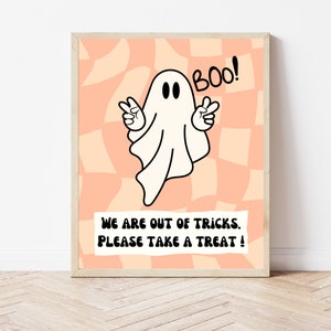 Op de afbeelding: Een printbaar Halloween-bord met een cartoon-spook met de tekst "Boo!" en de boodschap "We zijn uit de trucs. Neem een traktatie!" op een perzikkleurige en witte geruite achtergrond.