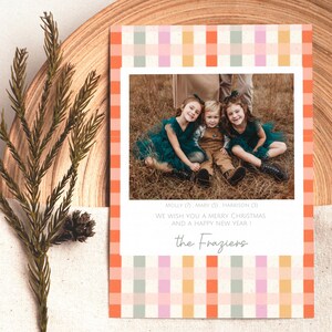 May include: A holiday card with a family photo, framed by a colorful plaid pattern in orange, pink, and green. The card includes the text "WE WISH YOU A MERRY CHRISTMAS AND A HAPPY NEW YEAR!" and the family name "the Fraziers".