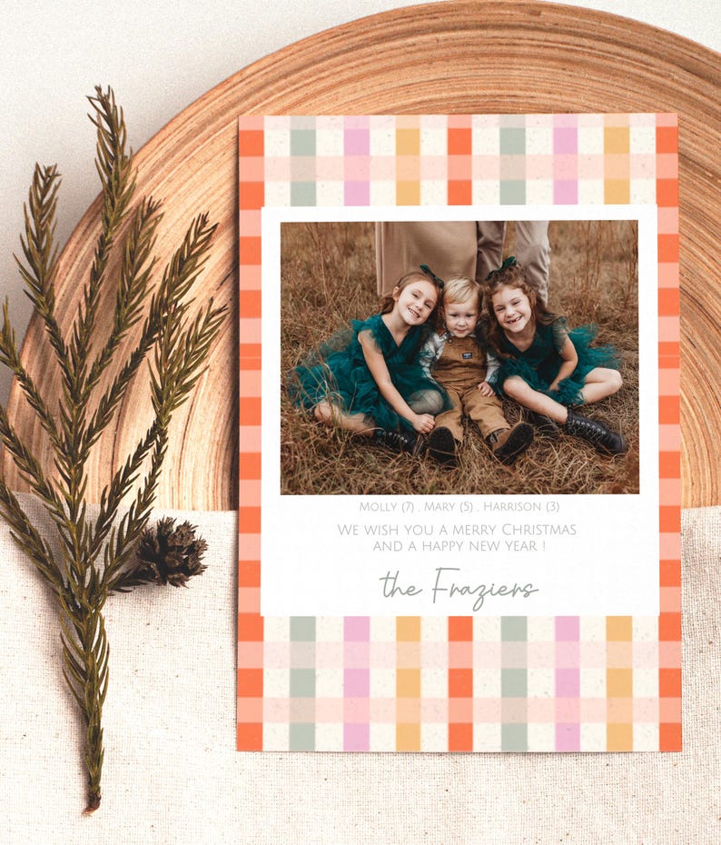 May include: A holiday card with a family photo, framed by a colorful plaid pattern in orange, pink, and green. The card includes the text "WE WISH YOU A MERRY CHRISTMAS AND A HAPPY NEW YEAR!" and the family name "the Fraziers".