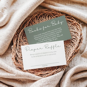 May include: Two cards for a baby shower, one sage green and one white, rest on a woven basket. The green card reads "Books for Baby" and the white card says "Diaper Raffle". Both cards have elegant script.