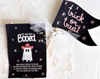 May include: Black Halloween-themed decorations. One is a flag with "trick or treat" in pink script, surrounded by stars. The other is a card with a ghost wearing a cowboy hat and the words "You have been Booed". Text on the card explains the Halloween tradition.