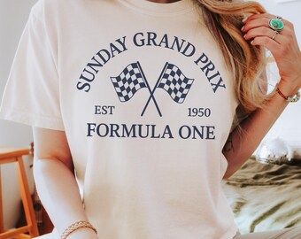 May include: Cream-colored t-shirt with the text "SUNDAY GRAND PRIX FORMULA ONE EST 1950" and crossed checkered flags. The shirt is short-sleeved and has a crew neck. The overall theme is Formula One racing.