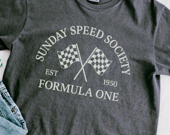 Puede incluir: Camiseta gris oscuro con el texto "SUNDAY SPEED SOCIETY" y "EST 1950 FORMULA ONE" en un diseño circular. Dos banderas a cuadros cruzadas están en el centro. La camiseta es de cuello redondo.
