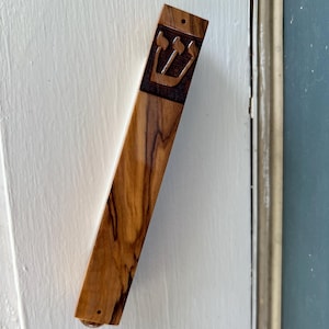 May include: A wooden mezuzah with a carved Star of David design. The mezuzah is attached to a white door frame.
