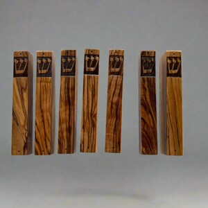 May include: Seven wooden mezuzah cases with a Hebrew inscription. The cases are made of olive wood and have a natural wood finish.
