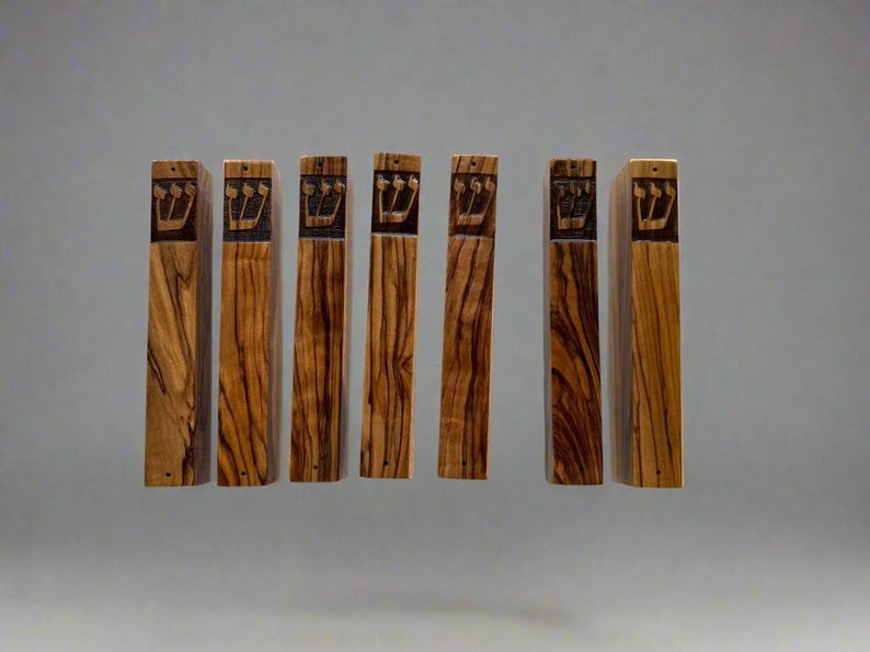 May include: Seven wooden mezuzah cases with a Hebrew inscription. The cases are made of olive wood and have a natural wood finish.