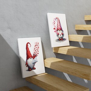 May include: Two white canvases with red and white gnomes holding letters with hearts floating around them. The canvases are on a wooden staircase.