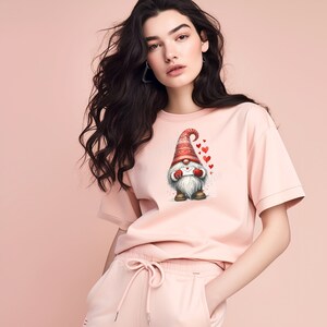 May include: A pink t-shirt with a cartoon gnome holding a letter and surrounded by red hearts. The gnome is wearing a red hat with white trim.