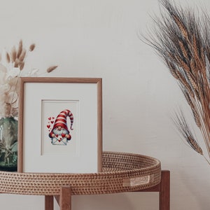 May include: A framed illustration of a gnome wearing a red and white striped hat holding a red envelope with hearts. The gnome is surrounded by small red hearts.