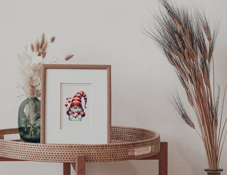 May include: A framed illustration of a gnome wearing a red and white striped hat holding a red envelope with hearts. The gnome is surrounded by small red hearts.