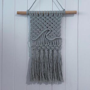 May include: A grey macrame wall hanging with a wave design and fringe tassels.