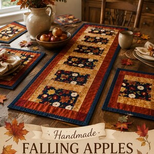 May include: A rectangular table runner and matching placemats featuring a patchwork design with dark blue fabric printed with apples and autumn leaves, bordered by gold and rust-colored fabric. The text reads: Handmade FALLING APPLES TABLE RUNNER Ready to ship! MATCHING PLACEMATS!