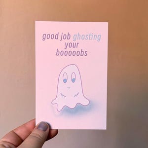 May include: A greeting card with a light pink background and a cartoon ghost illustration. The text on the card reads "good job ghosting your booooobs". The ghost has blue eyes and stitched details.