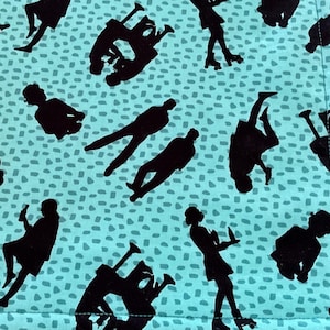 Può includere: Un tessuto turchese con un motivo ripetuto di figure nere di pattinaggio a rotelle e forme astratte. Il tessuto ha un bordo azzurro e uno sfondo maculato.