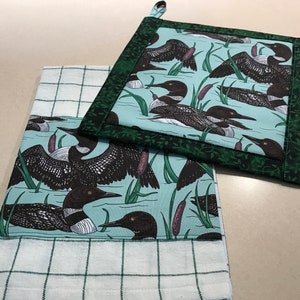 以下が含まれることがあります： 緑と青のチェック柄のキッチンタオル2枚。1枚は緑色の縁取りがあり、薄い青色の背景に黒と白の loon 鳥が繰り返し描かれたパターンがあります。もう1枚は白い縁取りがあり、薄い青色の背景に黒と白の loon 鳥が繰り返し描かれたパターンがあります。