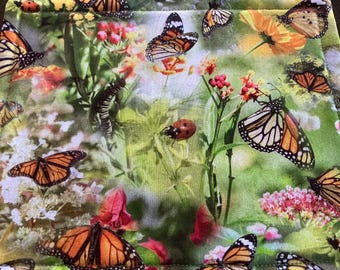 Tapete para aperitivos hecho a mano con hermosas mariposas monarca, orugas, mariquitas y flores sobre follaje en tonos verdes.