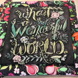 May include: Black and white fabric pot holder with a floral design and the text "What a wonderful world" written in white chalk.