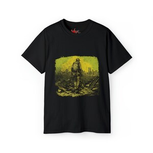 以下が含まれることがあります： 破壊された街を歩く人のグラフィックプリントが施された黒いTシャツ。グラフィックは緑と黄色の色合いです。