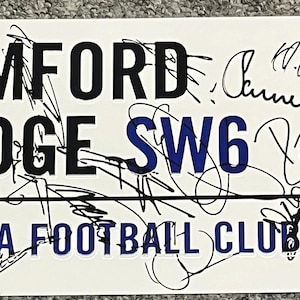 May include: A rectangular white sign with black text that reads "STAMFORD BRIDGE SW6" and "CHELSEA FOOTBALL CLUB". The sign also features the Chelsea Football Club logo and several signatures. The sign is likely a collectible item.