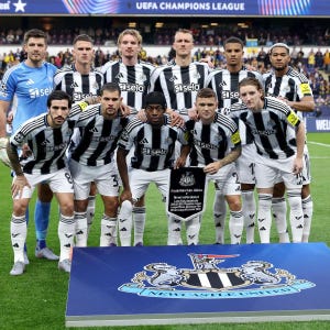 May include: A group of soccer players in black and white striped jerseys and white shorts pose for a photo. The team is holding a plaque with text. The background includes a stadium and the words "UEFA CHAMPIONS LEAGUE".
