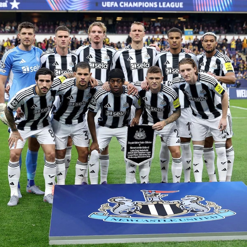 May include: A group of soccer players in black and white striped jerseys and white shorts pose for a photo. The team is holding a plaque with text. The background includes a stadium and the words "UEFA CHAMPIONS LEAGUE".