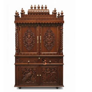 May include: A tall, dark brown wooden cabinet featuring intricate carvings on two upper doors and two lower doors. The upper section has a decorative top with small finials. The lower section includes a drawer and two doors with relief carvings of a peacock and figures.