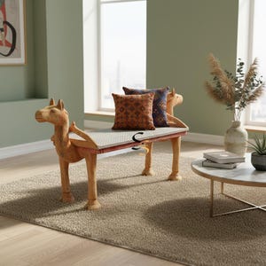 May include: A wooden bench featuring carved camel-shaped ends with a light-colored seat cushion. Two square throw pillows are placed on the bench, one in a burnt orange with a geometric pattern and the other in a dark blue with a similar pattern.