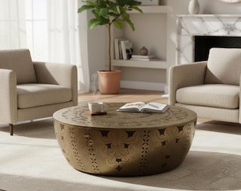 May include: A round, drum-shaped coffee table crafted from brass-toned metal, featuring an intricate, embossed floral and geometric pattern across its surface. The table has a low-profile design with a wide, cylindrical base and a flat top.