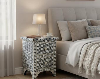 May include: A rectangular bedside table featuring two drawers with a black and white geometric floral inlay pattern. The table has a flat top surface, four short legs, and two small round knobs centered on each drawer front.