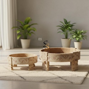 May include: Two round, light-colored wooden low tables featuring intricate, hand-carved floral and geometric patterns along the sides and legs. The tables have a natural wood finish with subtle red accents within the carved details.
