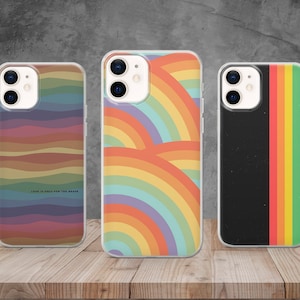 Puede incluir: Tres fundas transparentes para teléfono con diferentes diseños. La primera funda tiene un patrón de arcoíris con el texto "Love is only for the brave". La segunda funda tiene un patrón de arcoíris con un diseño más abstracto. La tercera funda tiene un fondo negro con un patrón de rayas de arcoíris.