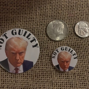 May include: Two round buttons with a white background and black text that reads "NOT GUILTY". The buttons feature a photo of Donald Trump. The larger button is 2.25 inches in diameter and the smaller button is 1.25 inches in diameter.