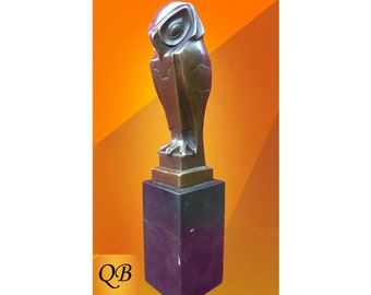 May include: A bronze sculpture of an owl perched on a black square base. The owl is stylized with geometric shapes and has a large, round eye. The sculpture is on a bright orange background with the letters "Q B" in the lower left corner.