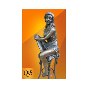 May include: Bronze sculpture of a woman sitting on a stool. The woman is wearing a flowing dress and has her hair pulled back. The sculpture is set against a bright orange background.