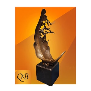May include: Bronze feather sculpture with a black base. The feather design features intricate details and a stylized figure at the top, with several bird figures. The sculpture is set against an orange background. The letters "QB" are in the lower left corner.