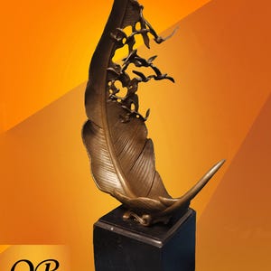 May include: Bronze feather sculpture with a flock of birds in flight, mounted on a black square base. The feather has detailed veining and a curved tip. The background is a gradient of orange and yellow.