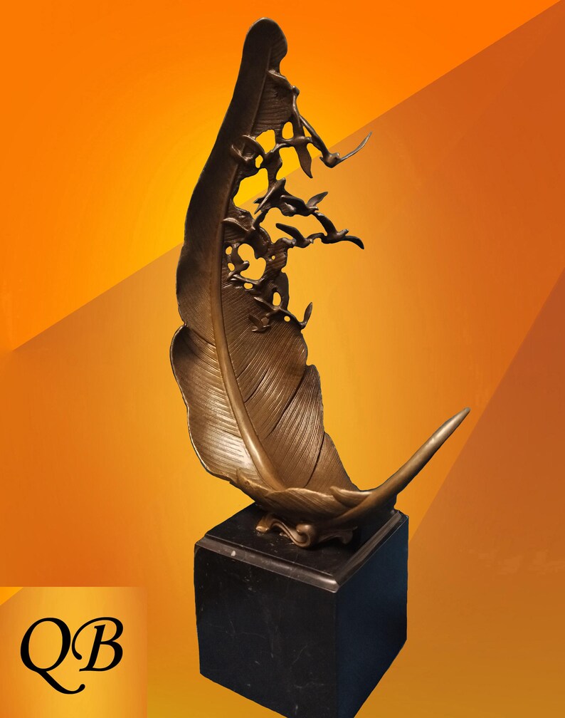 May include: Bronze feather sculpture with a flock of birds in flight, mounted on a black square base. The feather has detailed veining and a curved tip. The background is a gradient of orange and yellow.