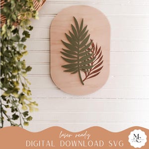 May include: Wooden wall art with a light brown oval base, featuring a green and brown leaf design. The text "laser ready DIGITAL DOWNLOAD SVG" is at the bottom. Suitable for home decor.