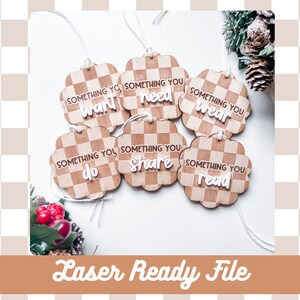 Puede incluir: Seis adornos de madera con un patrón a cuadros y texto blanco. El texto en los adornos dice "Something you want", "Something you need", "Something you wear", "Something you do", "Something you share", y "Something you read".