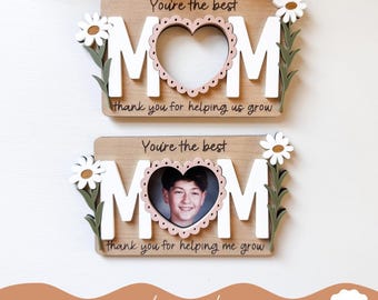 May include: Two wooden signs with the word "MOM" in white letters with a heart-shaped photo frame in the center. The top sign says "You're the best MOM thank you for helping us grow". The bottom sign says "You're the best MOM thank you for helping me grow".