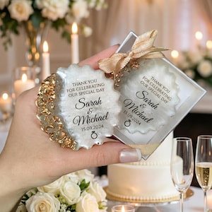 May include: Wedding favors with a gold and white design. The favors are shaped like a scalloped edge with gold accents and the text "Thank you for celebrating our special day" and the names "Sarah & Michael" with the date 15.09.2024.