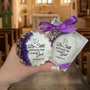 May include: Two decorative, white, scalloped-edge items with purple and gold accents. Each item has the text "Be Still, and know that I am God - Psalm 46:10" and a dove graphic. One is in a silver box with a purple ribbon.