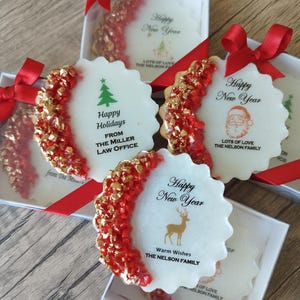 May include: Four round, scalloped-edge white ornaments in individual boxes with red ribbon bows. Each features a crescent of red and gold textured accents. Text includes Happy New Year, Happy Holidays, and family names like The Nelson Family.
