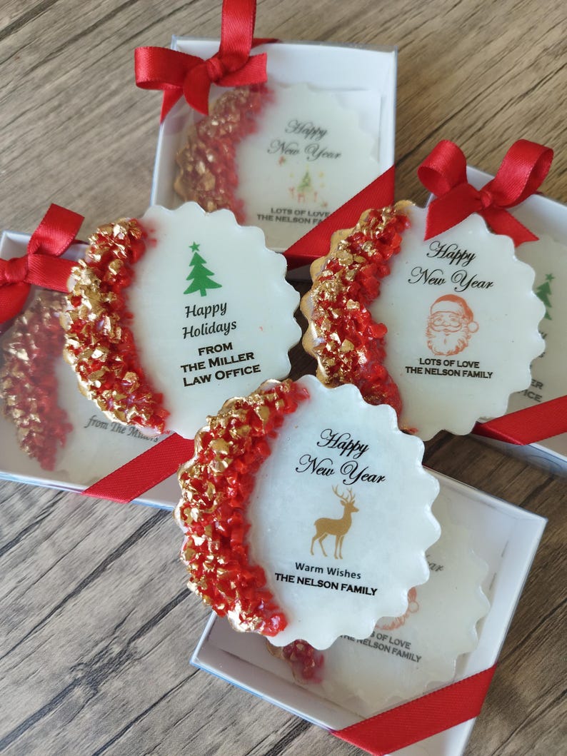 May include: Four round, scalloped-edge white ornaments in individual boxes with red ribbon bows. Each features a crescent of red and gold textured accents. Text includes Happy New Year, Happy Holidays, and family names like The Nelson Family.