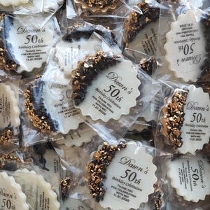May include: A collection of round, scalloped-edge white party favors individually wrapped in clear plastic. Each favor features black text reading Dawn's 50th Birthday Celebration, Thank You For Celebrating With Me, 11.21.2025, and a crescent-shaped accent of black and gold metallic flakes.