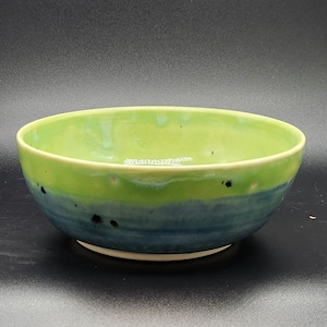 May include: A green and blue ceramic bowl with a speckled glaze. The bowl has a wide rim and a rounded bottom.