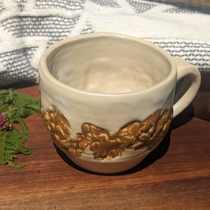 May include: A white ceramic mug with a brown, textured design. The mug has a rounded shape and a handle.