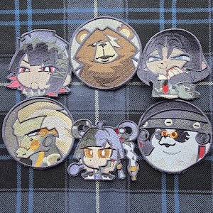 May include: A collection of six embroidered patches featuring stylised anime-inspired characters and a brown bear face. The patches include circular and custom-shaped designs with detailed stitching in various colours including black, grey, brown, and gold.